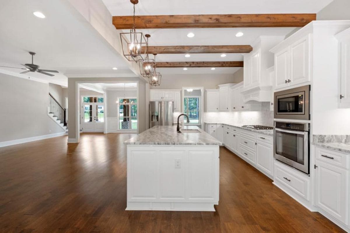 Open-concept kitchen with island, white cabinets, range, microwave, and decorative wood ceiling beams.