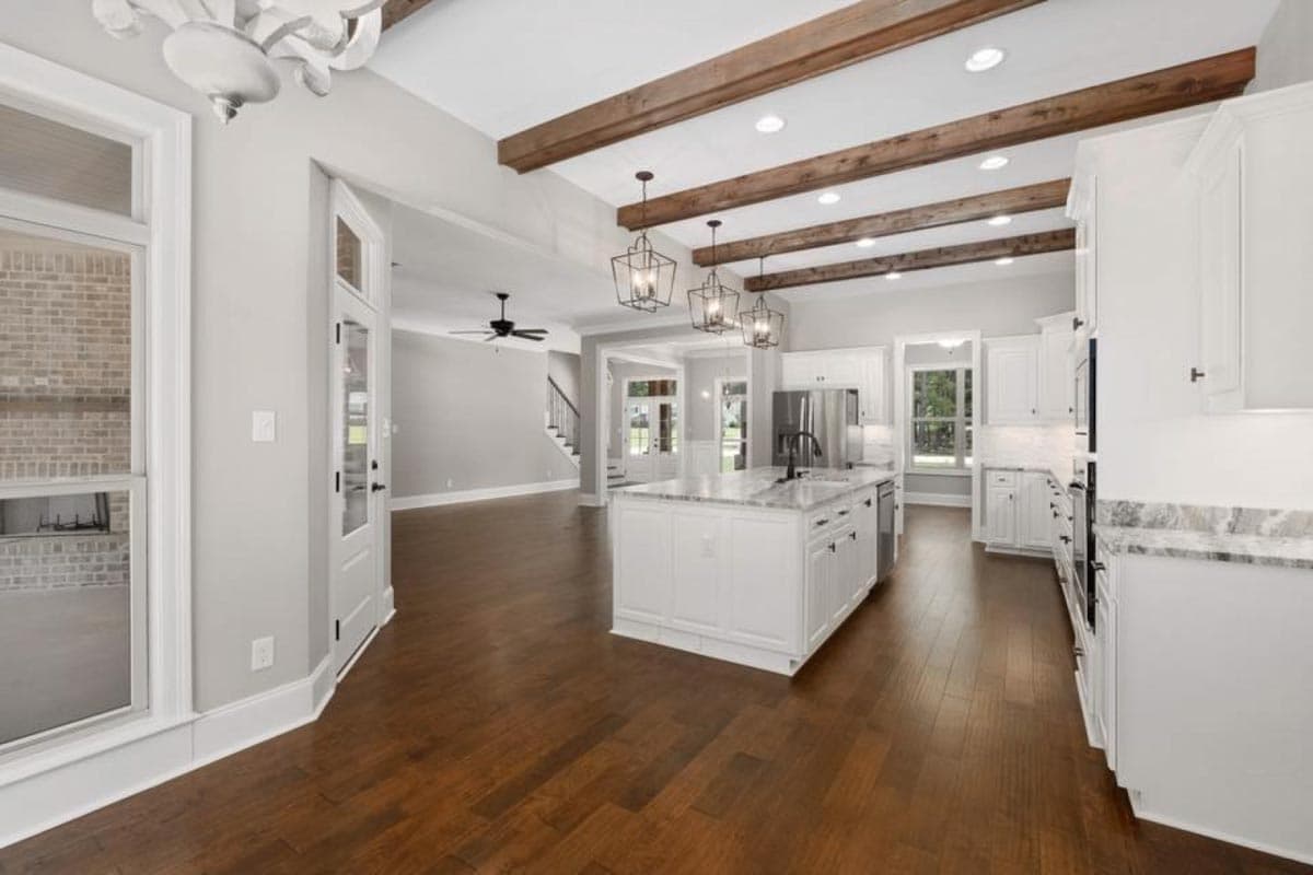 Open concept kitchen with island, white cabinets, and exposed wooden beams on vaulted ceiling.