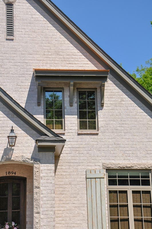 House plan exterior featuring white brick, dark gray trim, gable dormer with brackets, and multi-pane windows.