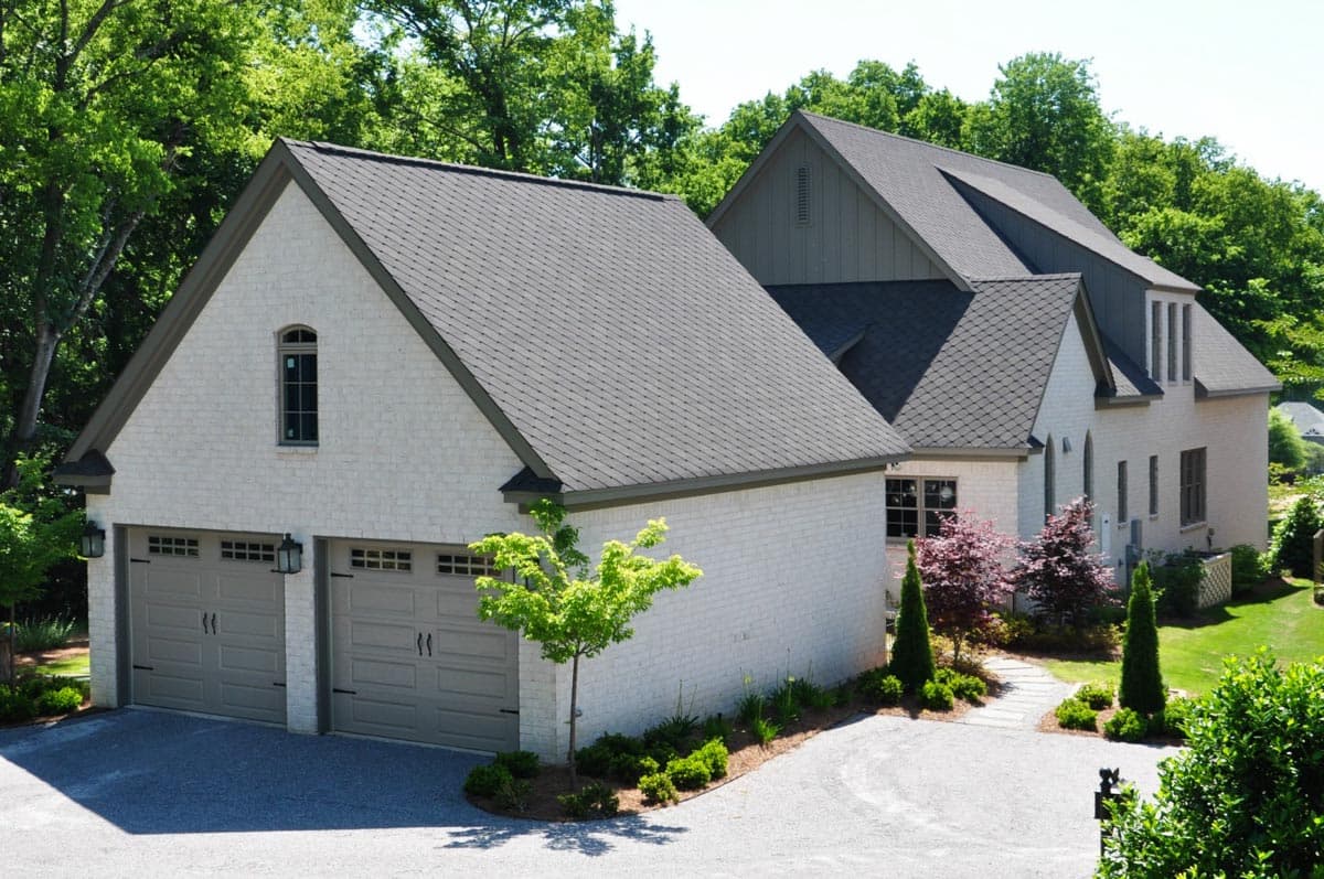 House plan exterior: White brick home with attached side-entry two-car garage, multiple gables, and dark asphalt roof.