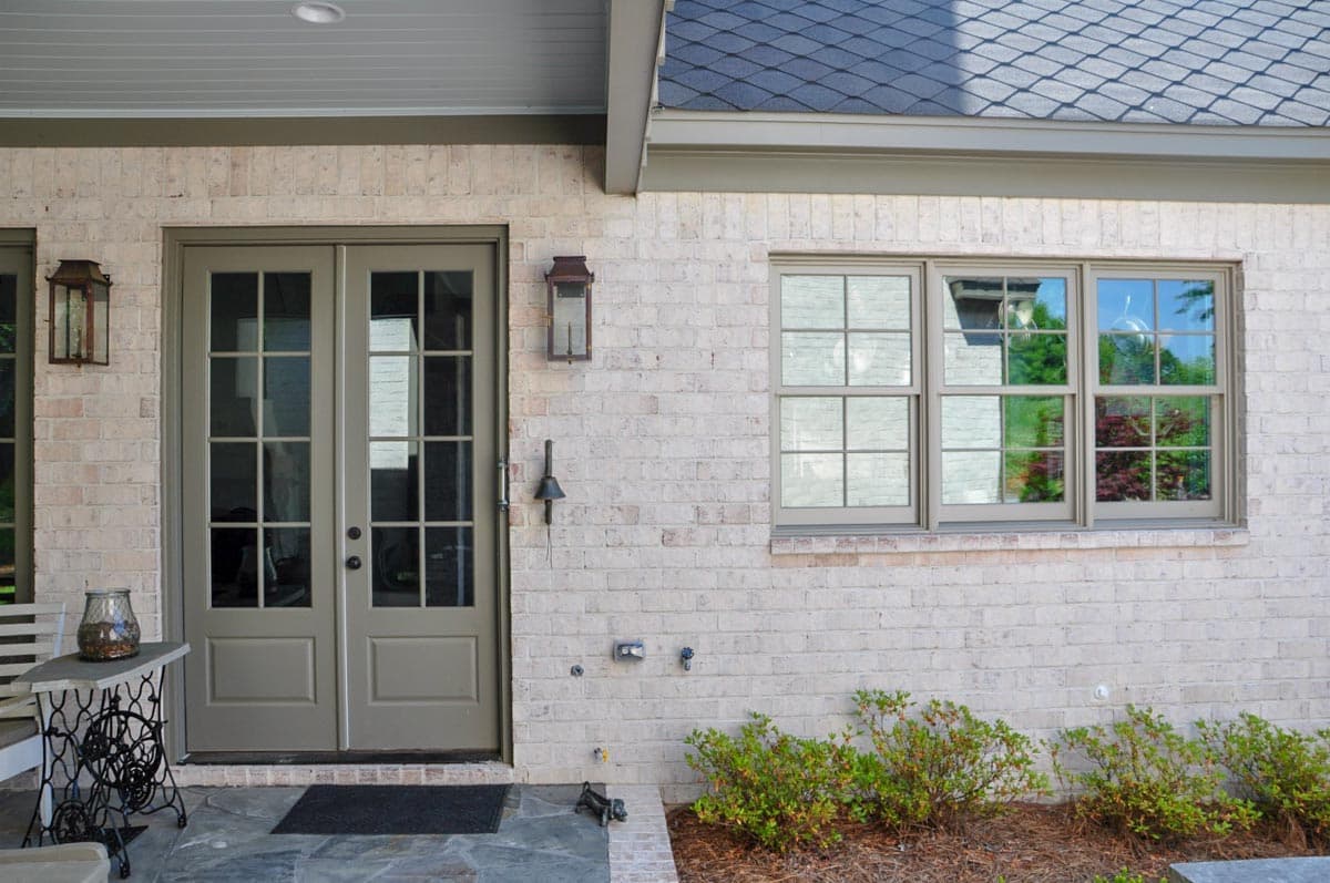 Exterior view of a house plan showing double glass doors, a multi-pane window, and light brick facade.