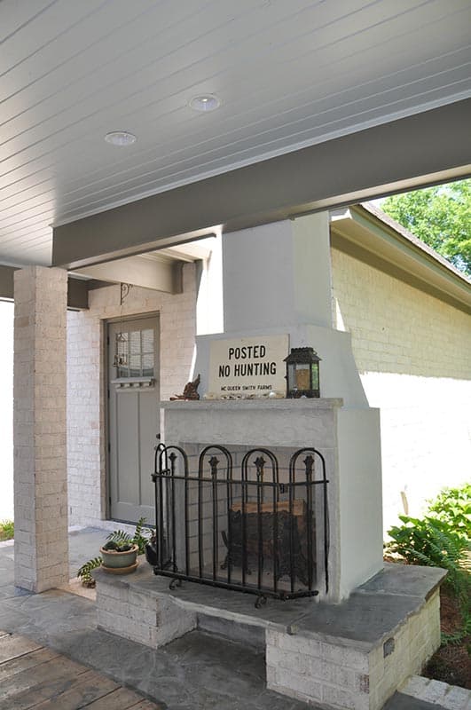 Porch exterior with white brick pillars, gray door, and a large white stucco fireplace with a "Posted No Hunting" sign.