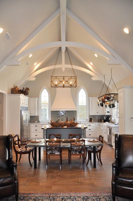 Kitchen with vaulted beamed ceiling, island with seating, arched windows, and stainless steel appliances.