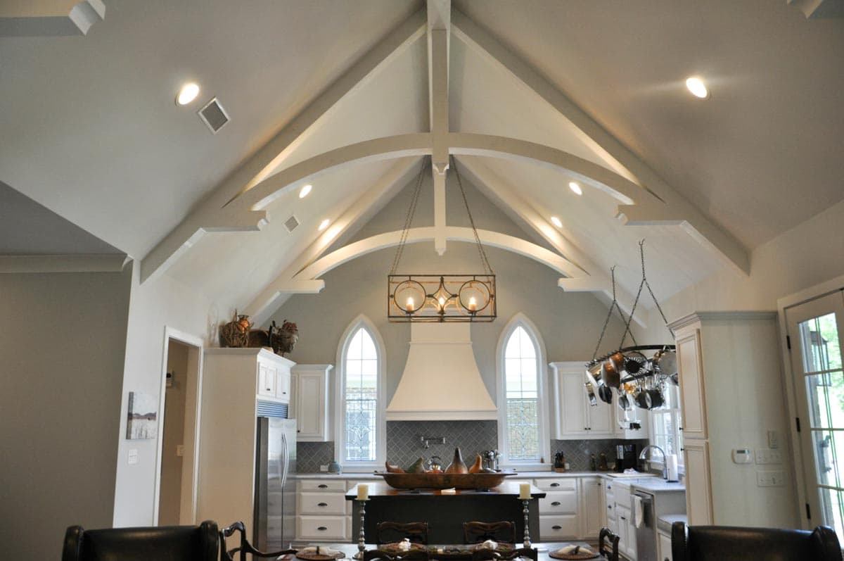 Kitchen with vaulted beamed ceiling, island, white cabinets, cathedral windows, and pendant lighting.
