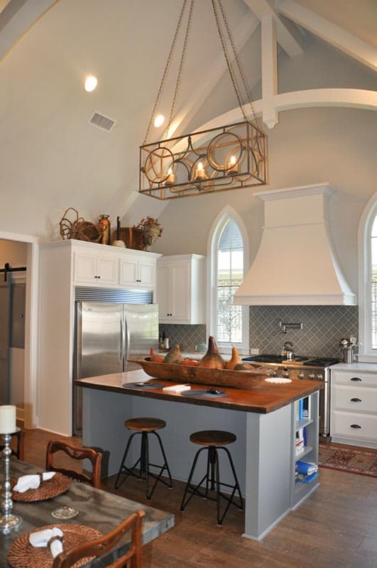 Kitchen with vaulted ceiling, central island with seating, stainless steel refrigerator, and decorative range hood.