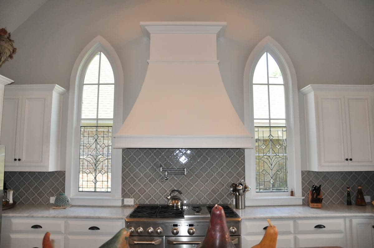 Kitchen with white cabinets, range hood, and Gothic-arch windows with decorative leaded glass.