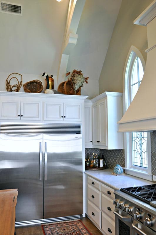 Kitchen with vaulted ceiling, stainless steel refrigerator, white cabinets, range, and arched window with stained glass detail.
