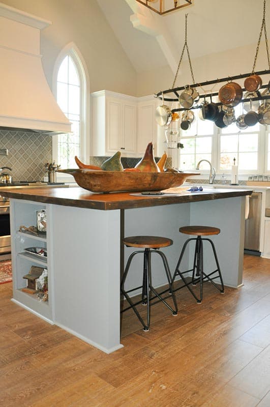 Kitchen with island, vaulted ceiling, large arched window, and pot rack.