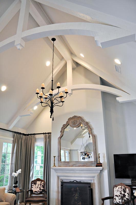 Vaulted ceiling with exposed beams, chandelier, and ornate mirror above fireplace.