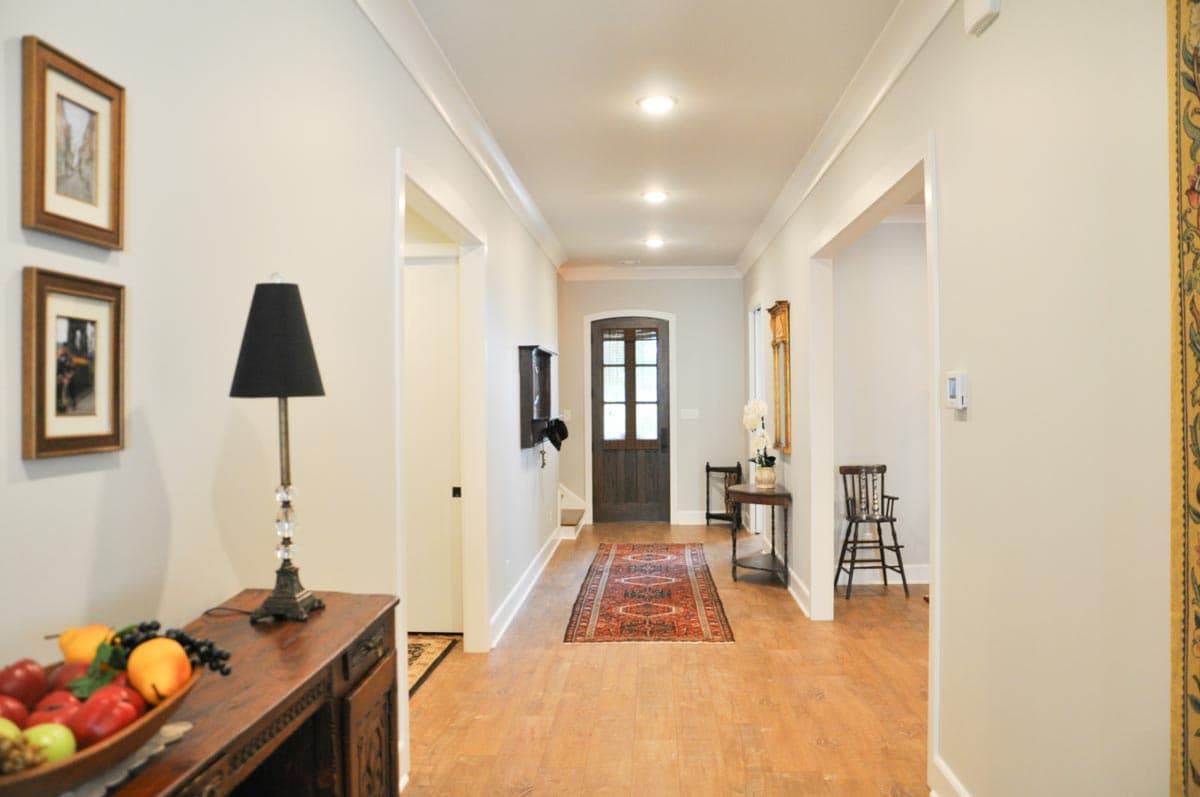 Interior hallway with hardwood floors, recessed lighting, and a dark wood door with glass panes. Features console tables and artwork.