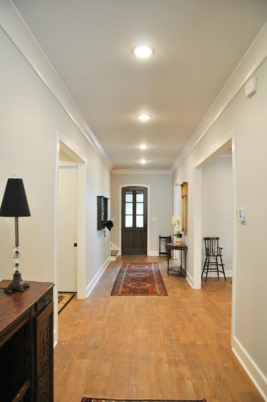 Hallway interior with hardwood floors, recessed lighting, a dark wood door with glass panes, and decorative runner rugs.