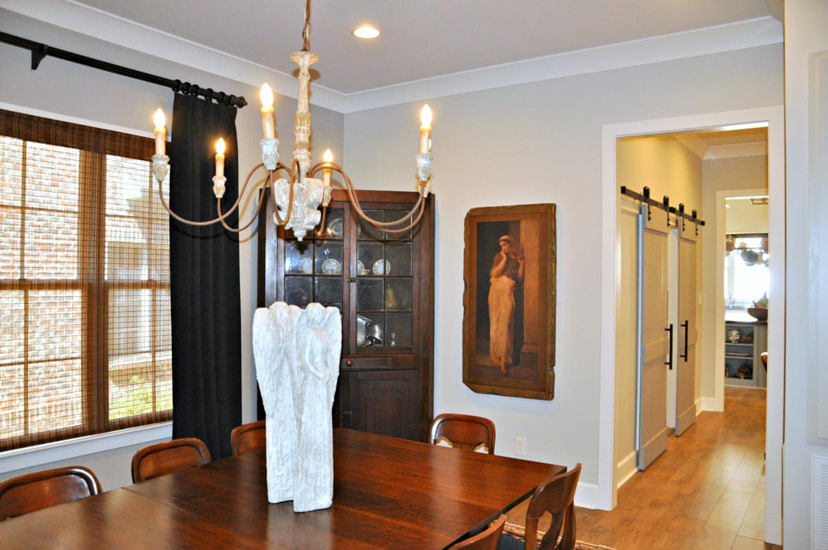 Dining room with dark wood table, six chairs, antique china cabinet, large window with blinds, and sliding barn doors leading to hallway.