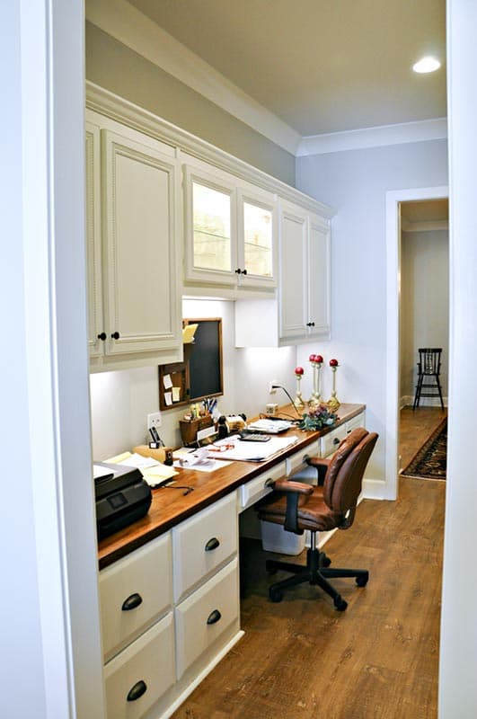 Home office with built-in desk, cabinetry, and illuminated display shelves.