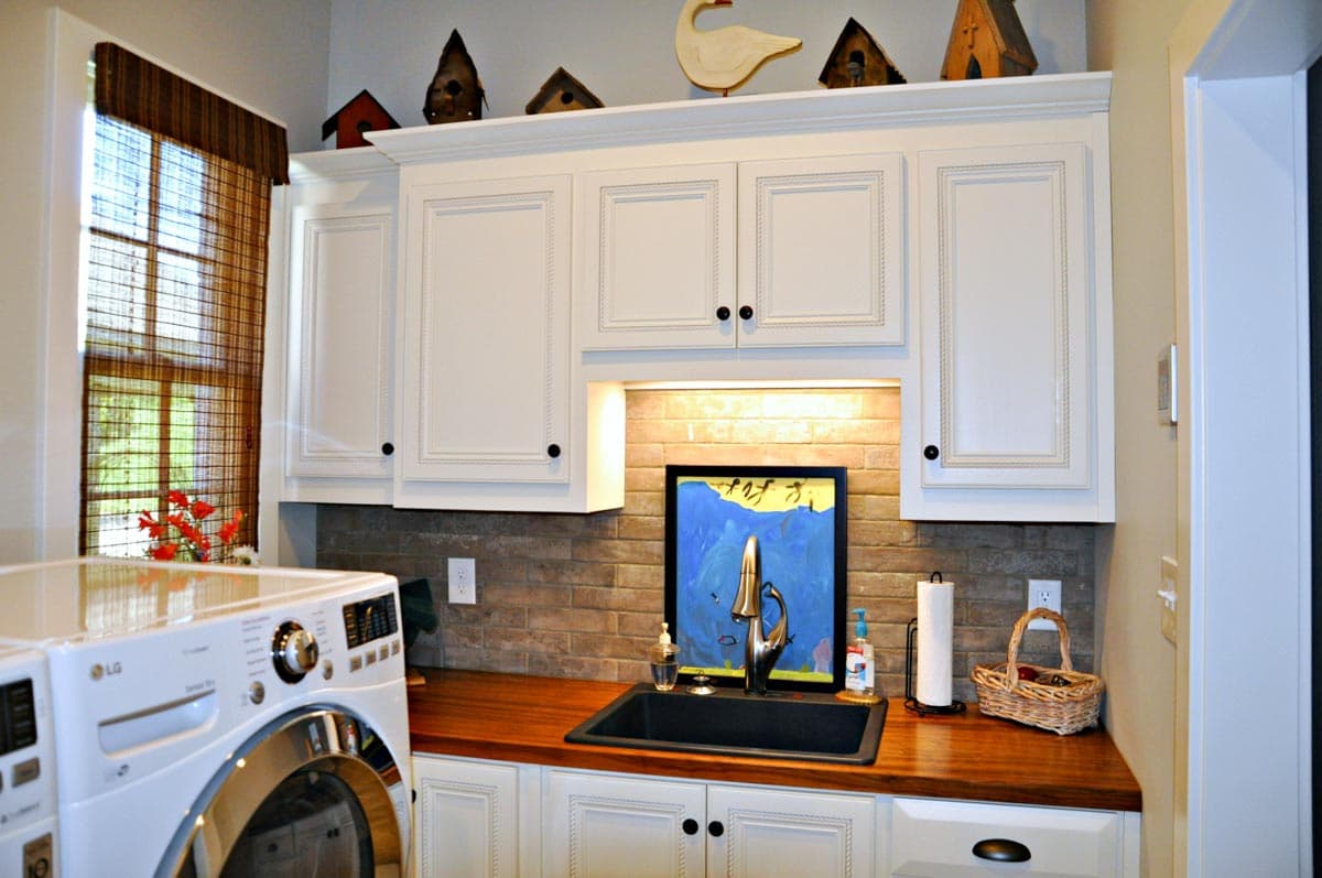 Laundry room with white cabinets, wood countertop, sink, washer, and window with bamboo blinds.