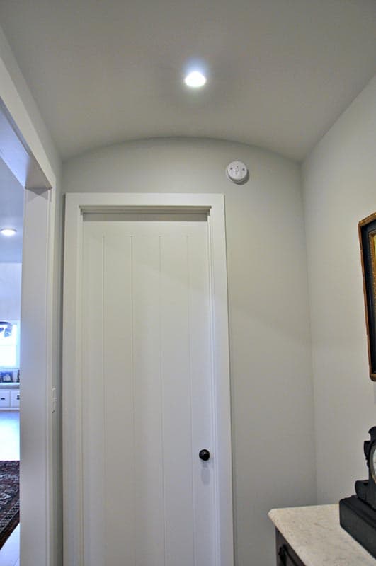 Interior view of a hallway with a paneled door, vaulted ceiling, and recessed lighting.