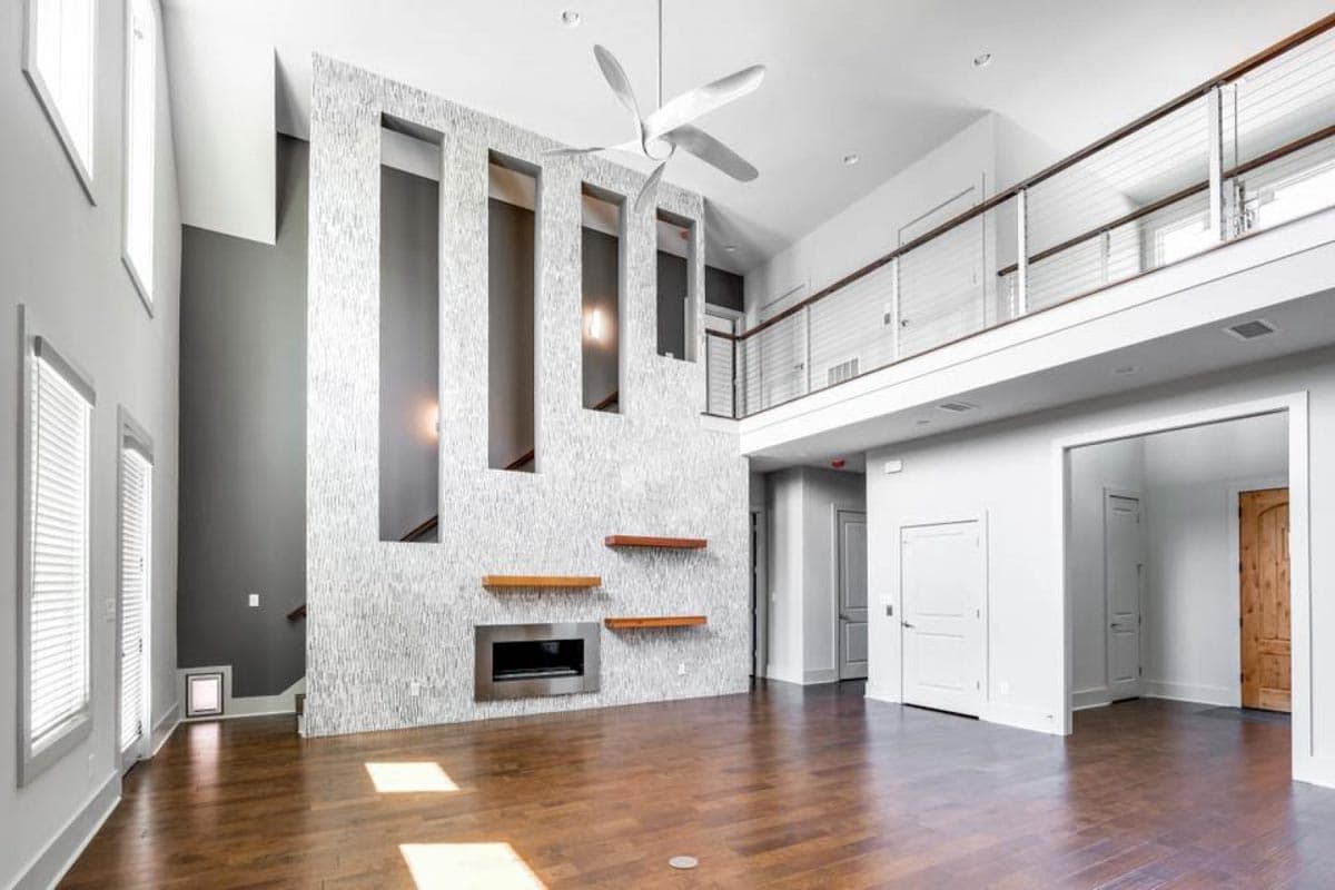 Interior rendering: Open living space with double-height ceiling, linear fireplace, modern railing, and wood floors.