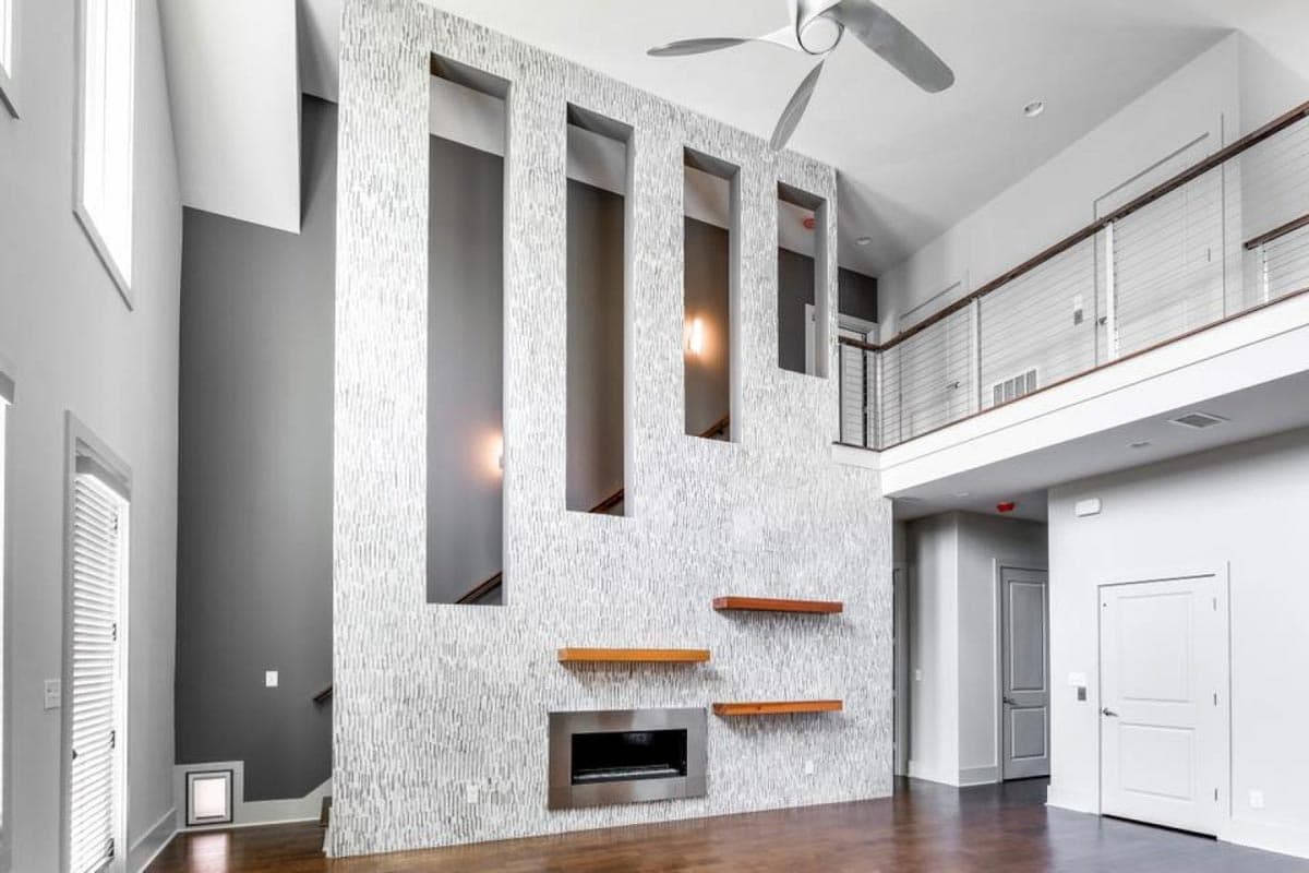 Interior view of a modern house with a two-story great room, textured accent wall, fireplace, and open loft.