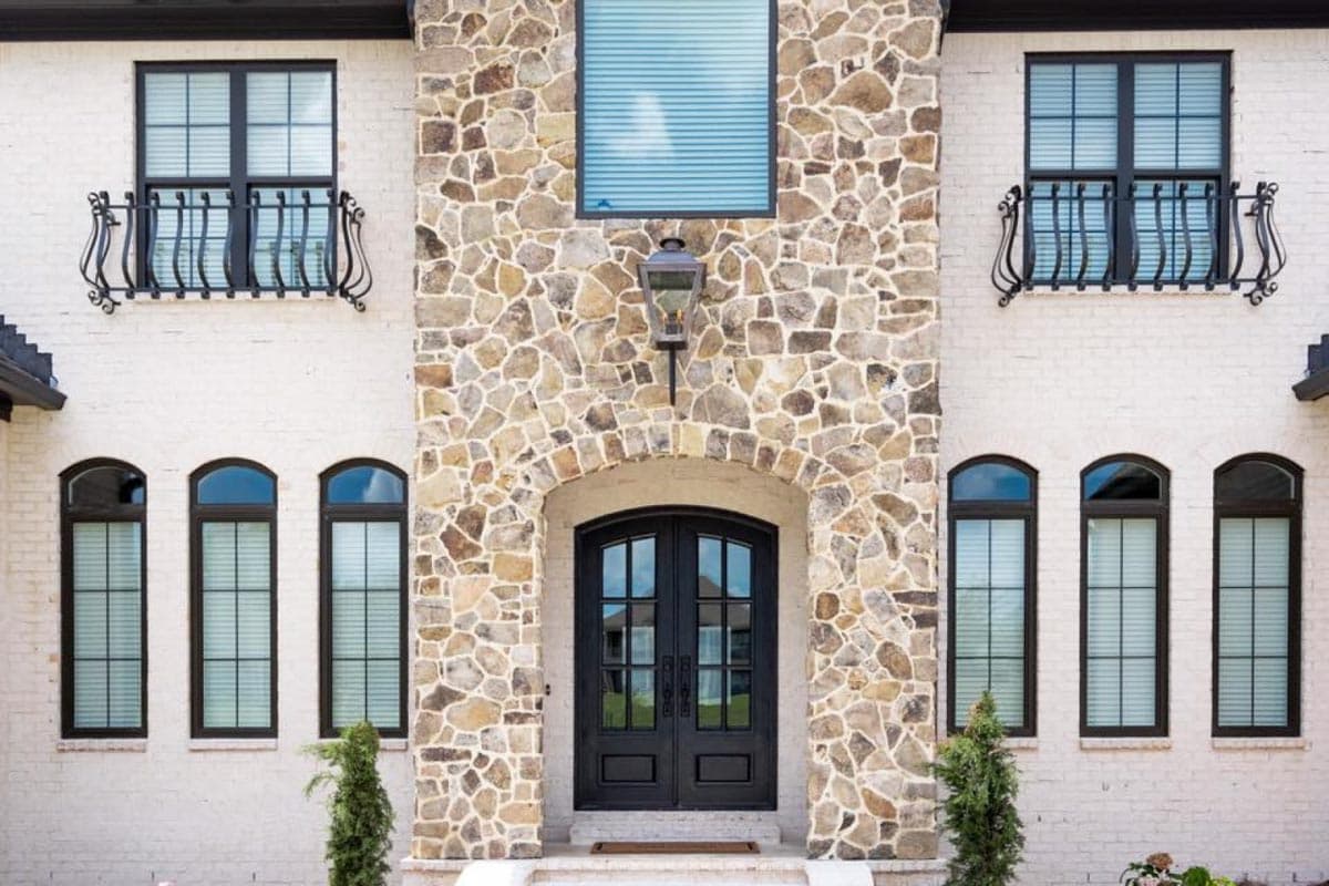 House plan exterior features arched stone entry with double doors, balconies on upper windows, and arched and rectangular windows.