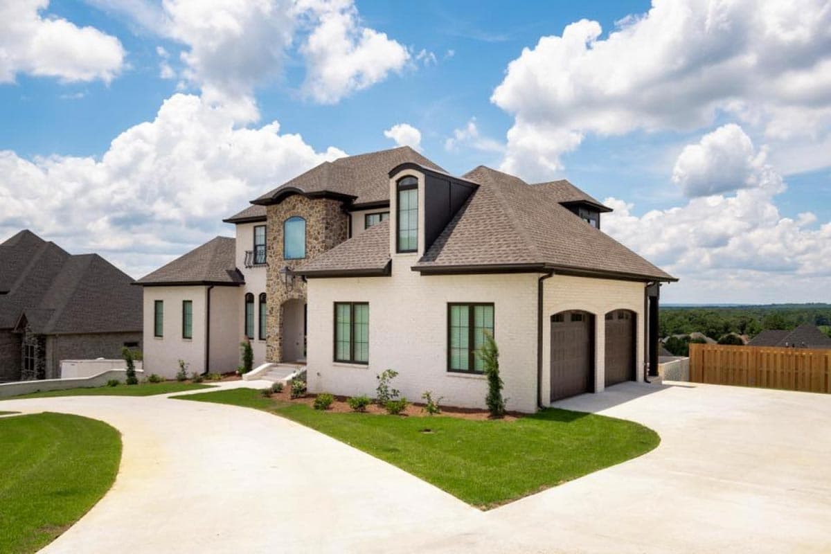 House plan exterior: Two-story home with stone accents, multiple gables, dormers, and a side-entry three-car garage.