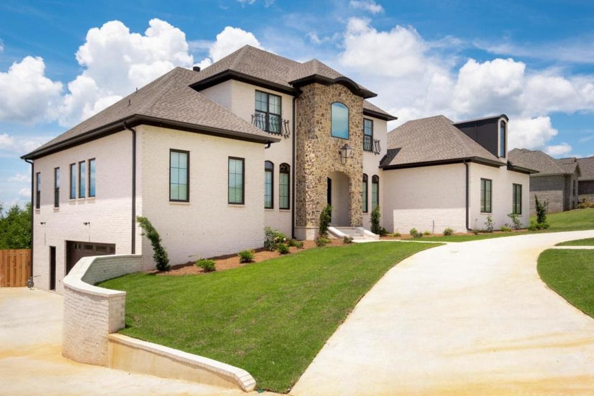 House plan exterior: Two-story home with white brick, arched stone entryway, multiple gables, and side-facing garage.
