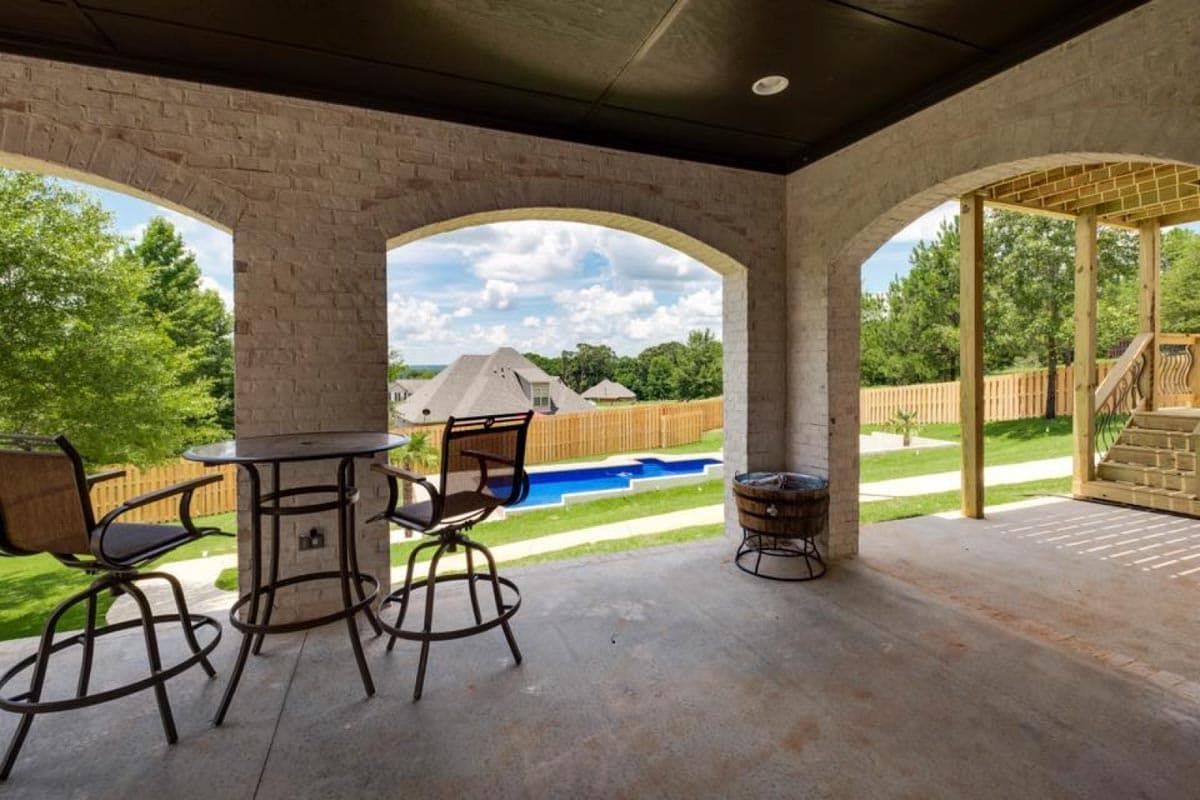 Covered porch with arched openings, brick pillars, bar seating, and view of pool and backyard.