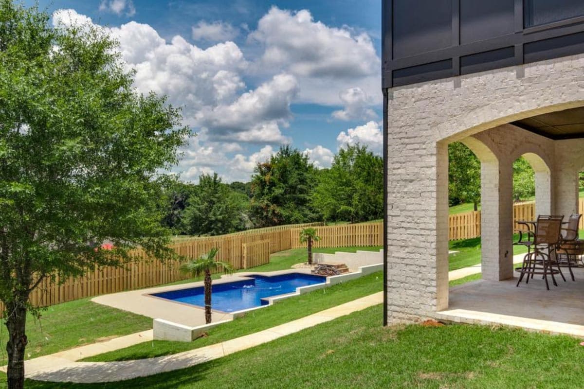 Exterior view of a Modern Farmhouse plan with a covered porch, white brick facade, and an in-ground pool.