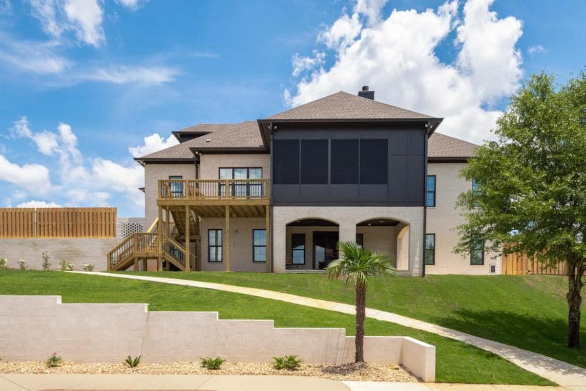 House plan exterior with a screened-in porch, wooden deck, and arched entryway on a sloped lawn.