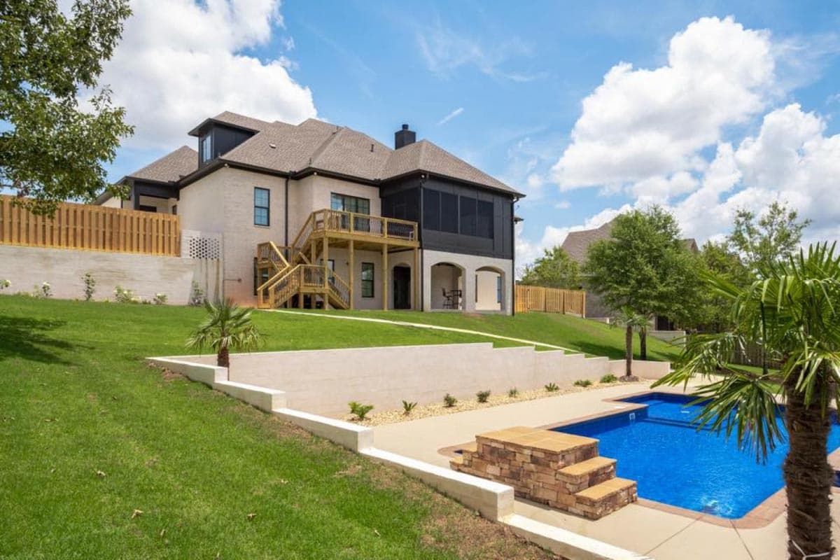 House plan exterior: two-story brick home with deck, screened porch, arched lower level, and a swimming pool.