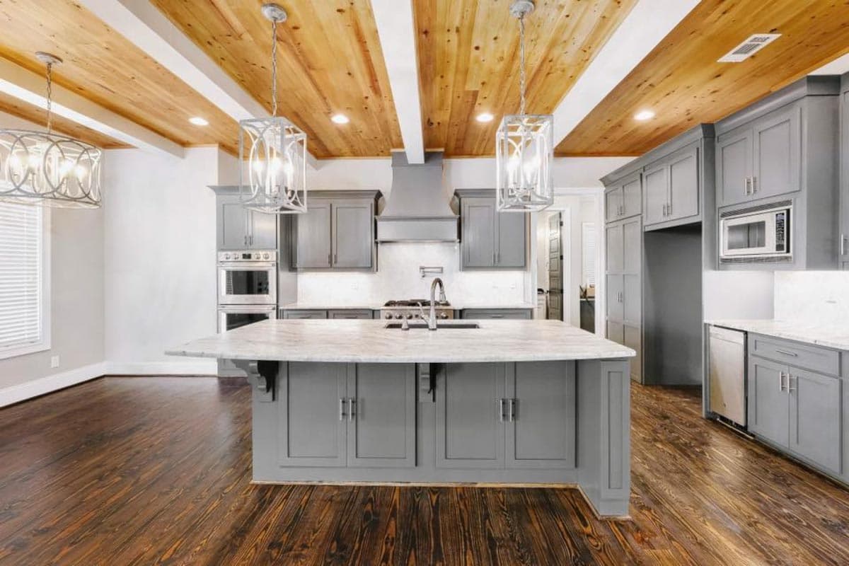 Kitchen with gray cabinets, marble island, stainless steel appliances, and wood-beamed ceiling.