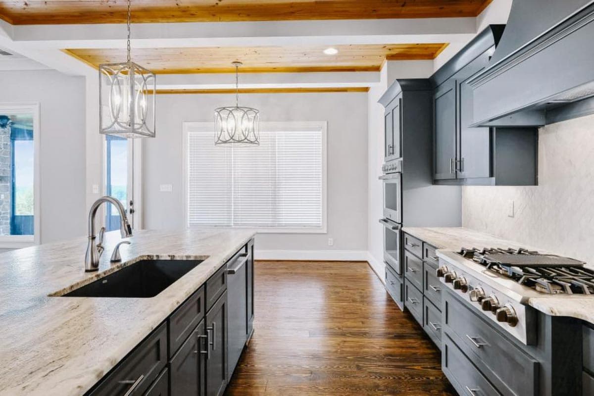Kitchen interior with coffered wood ceiling, island with sink, dark cabinets, built-in ovens, and gas range.