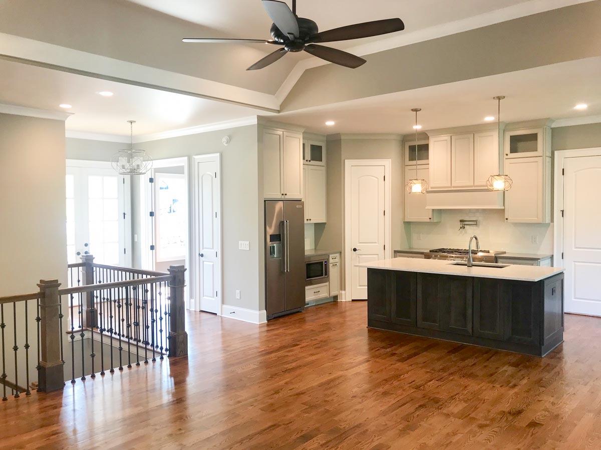 Open-concept kitchen with island, stainless steel appliances, white cabinetry, and vaulted ceiling with fan.
