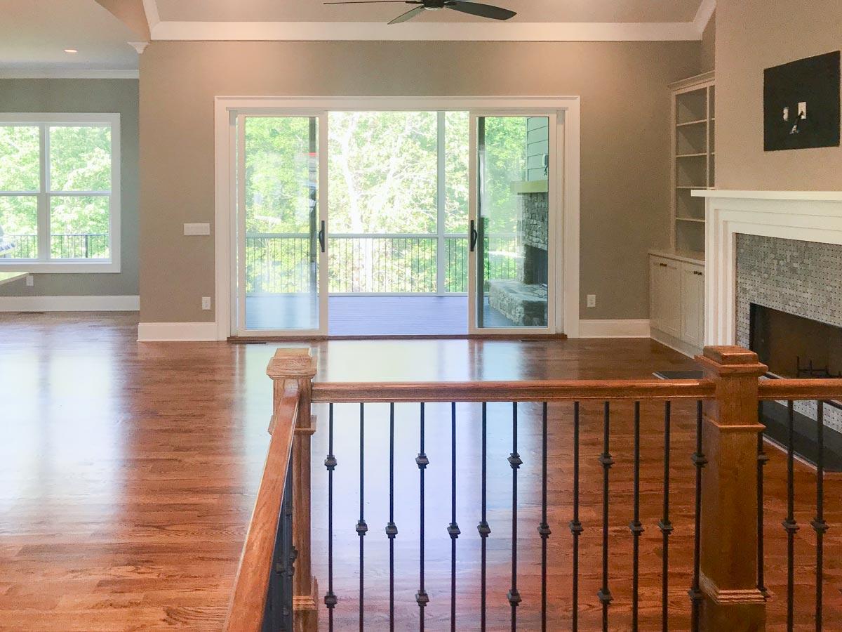 Interior view of open living space with large windows, sliding glass doors to deck, and stone fireplace with built-in shelving.