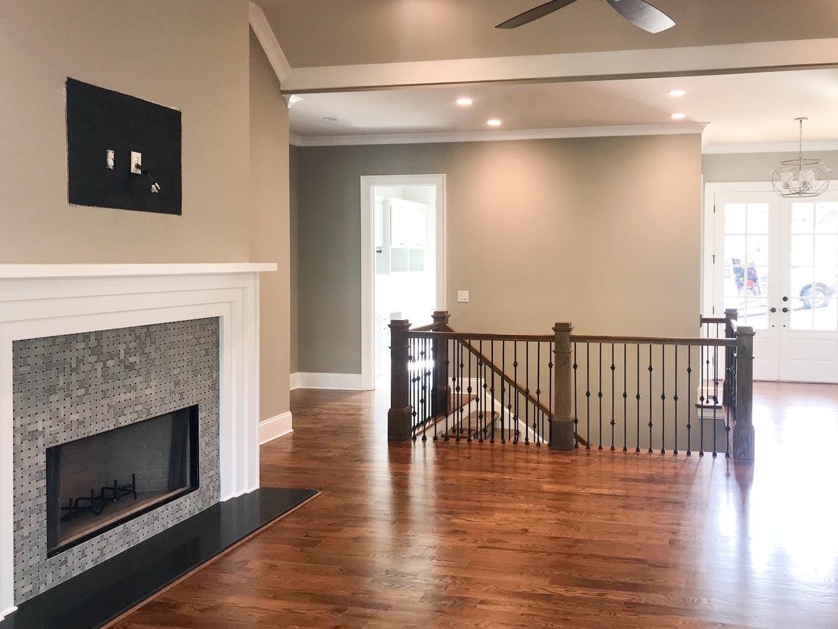 Interior view showing a fireplace with tiled surround, staircase with ornate railing, and an open floor plan leading to French doors.