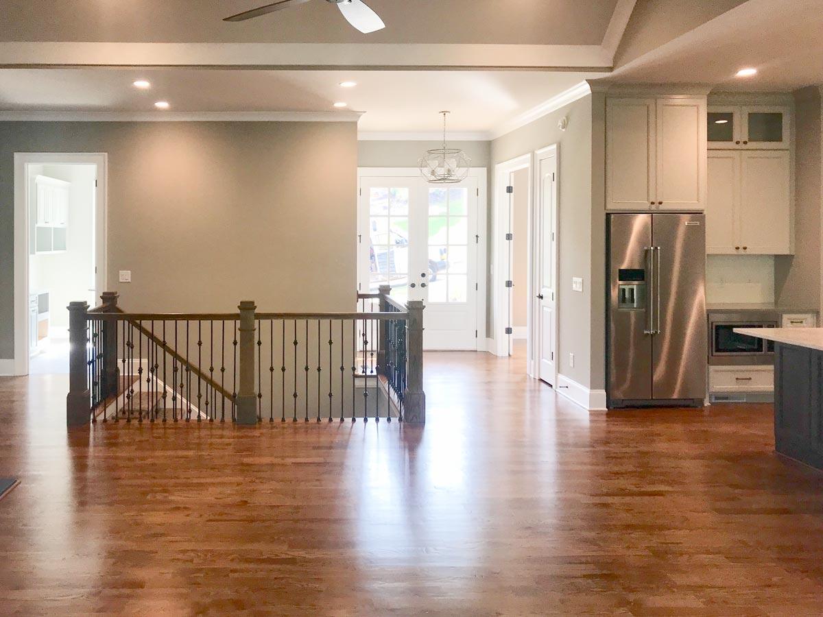 Interior view of open-concept living space with staircase, kitchen cabinets, and stainless steel refrigerator.