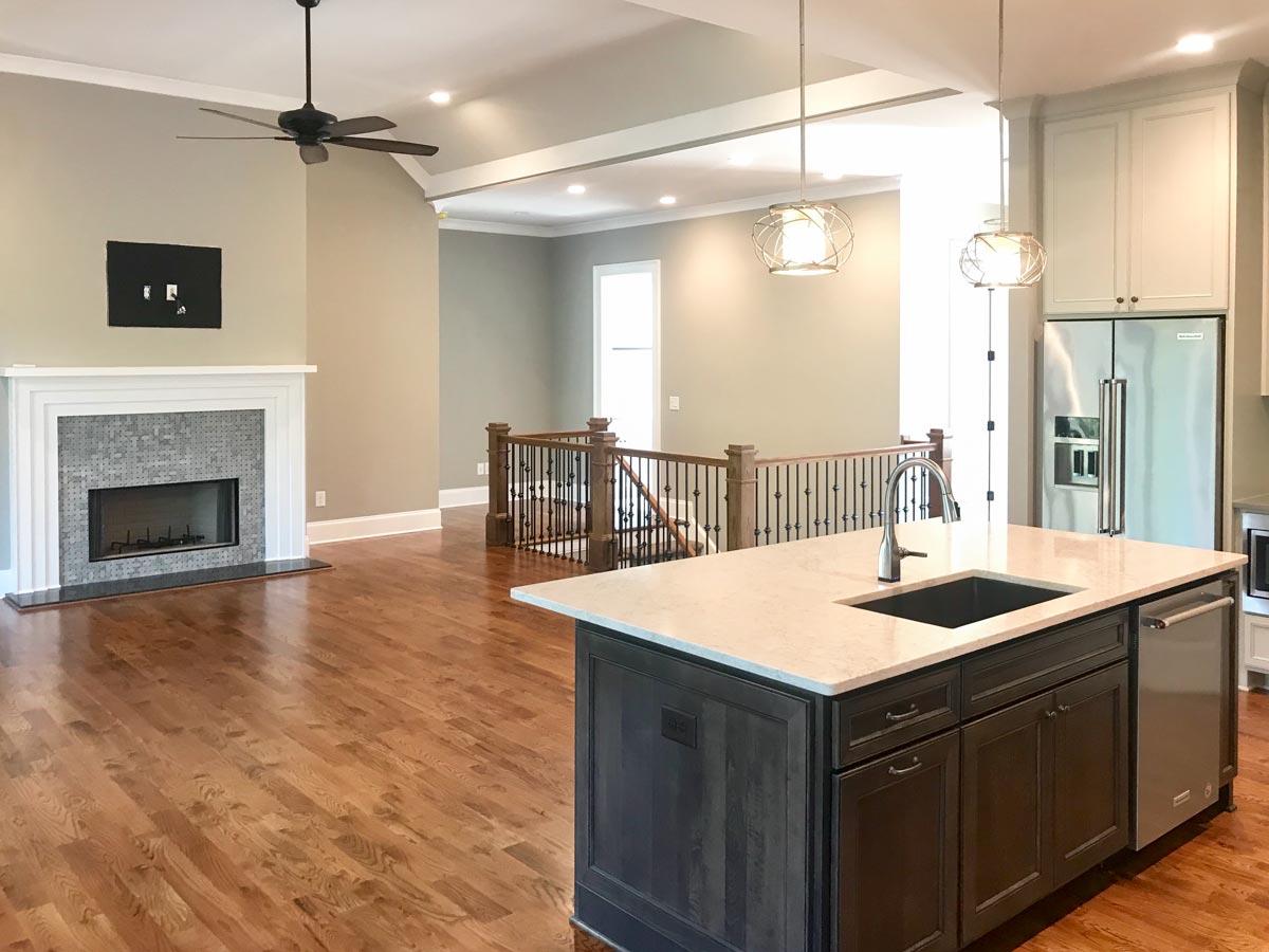 Interior view of open-concept living space with fireplace, kitchen island with sink, and vaulted ceiling.
