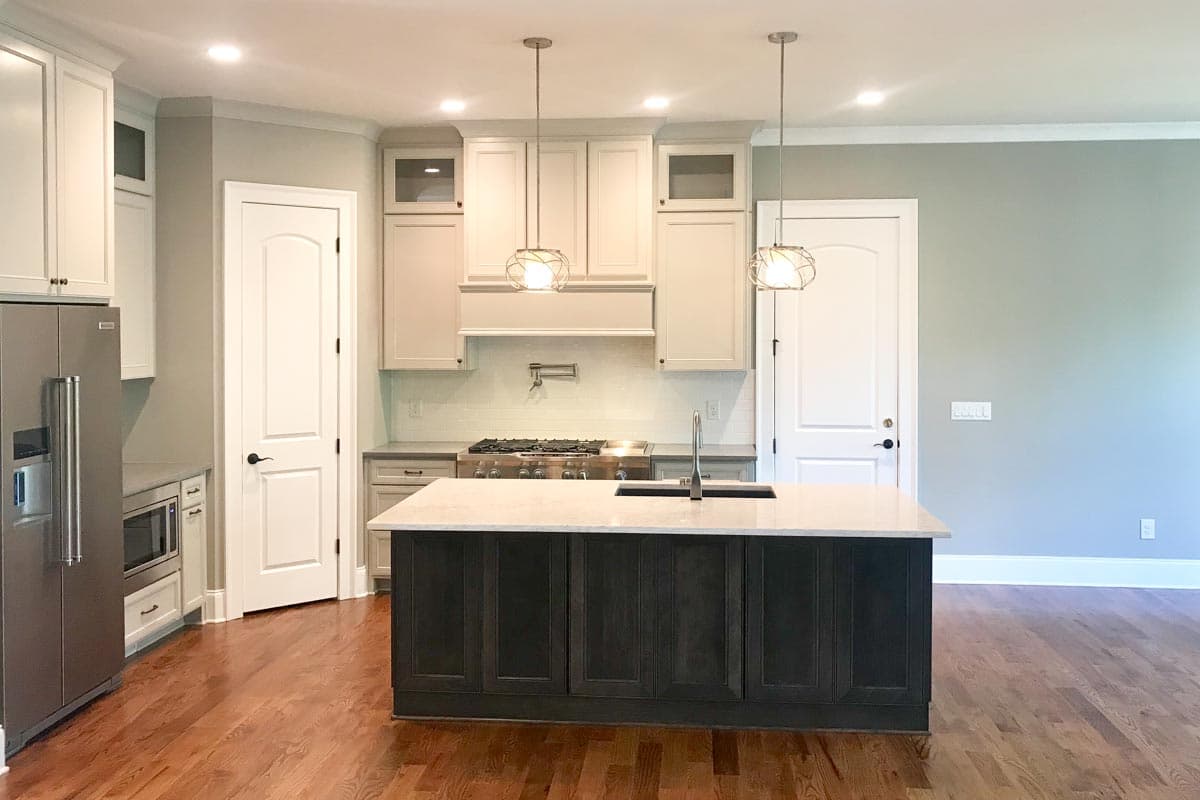 Kitchen with dark island, white cabinets, stainless steel appliances, gas range, pot filler, and pendant lights.