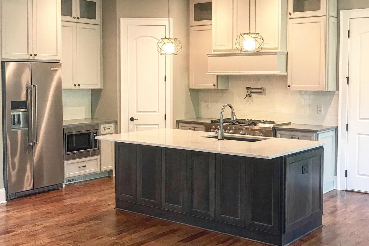 Kitchen with dark island, stainless steel refrigerator and microwave, range with hood, subway tile backsplash, and pendant lights.