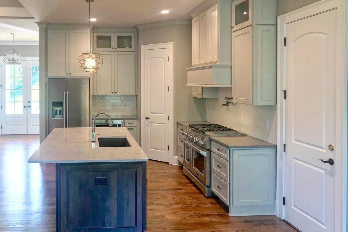 Kitchen with island, stainless steel refrigerator, range, and white cabinetry.