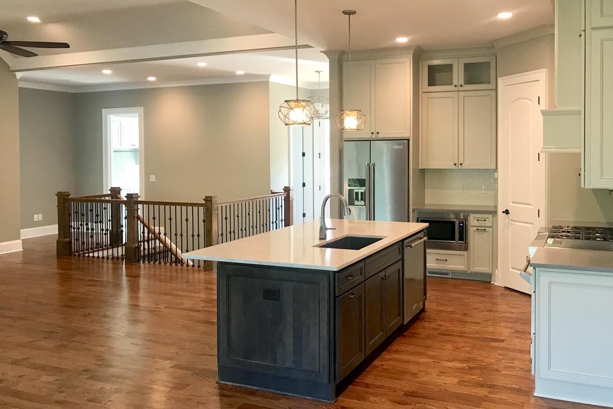 Open concept kitchen and living area with island, stainless steel appliances, and wood staircase with wrought iron railing.