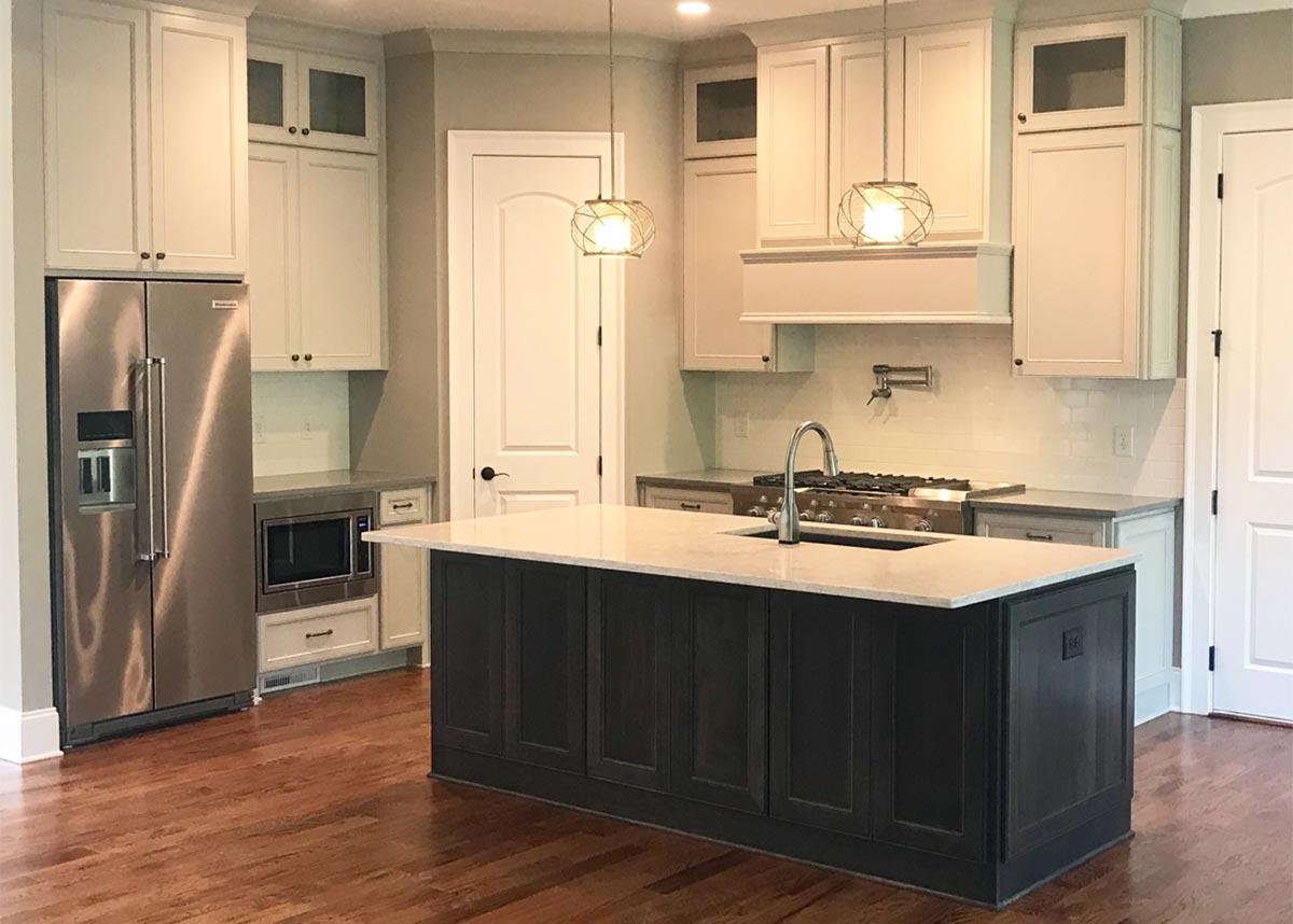 Kitchen with dark island, white perimeter cabinets, stainless steel refrigerator, microwave, and gas range.