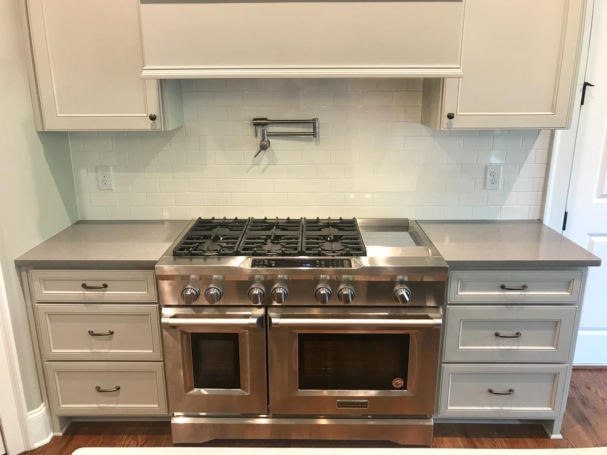 Kitchen featuring a stainless steel range with griddle, subway tile backsplash, gray countertops, and light gray cabinets with drawers.