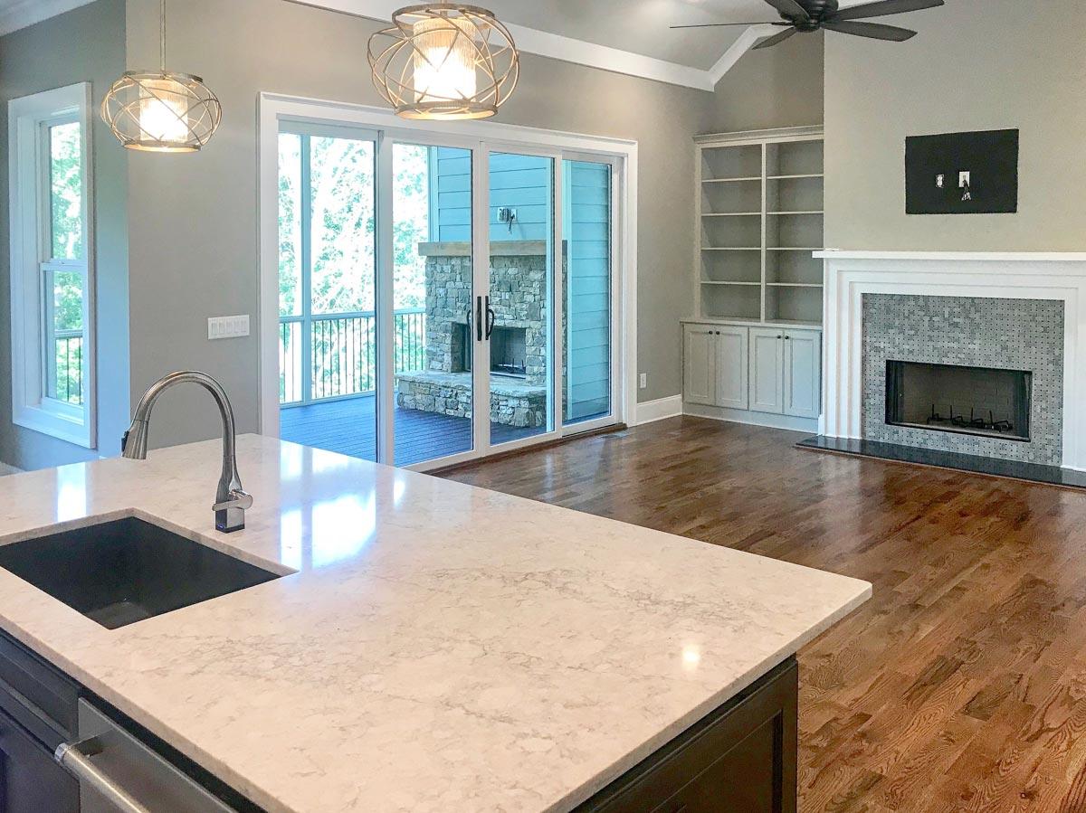 Open layout showcasing kitchen island with sink, fireplace with built-in shelving, and access to screened porch.