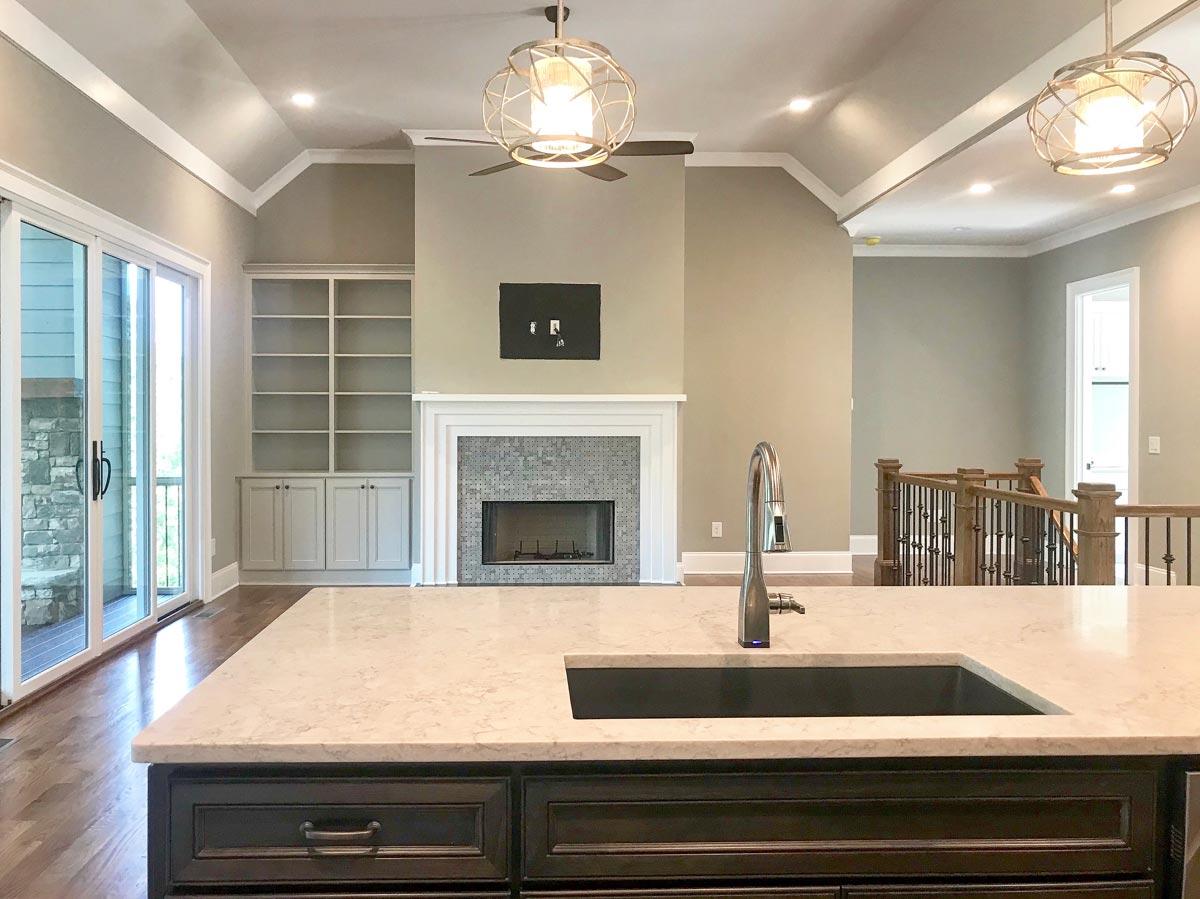 Kitchen island with sink and faucet overlooking a living area with fireplace, built-in shelving, and vaulted ceiling.