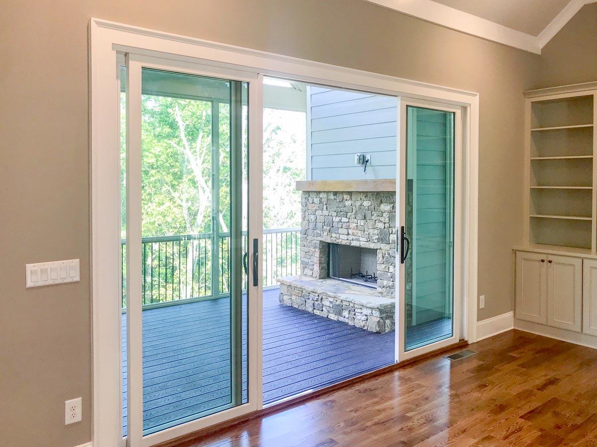 View through sliding glass doors to a screened porch with stone fireplace and deck. Built-in shelving unit to the right.