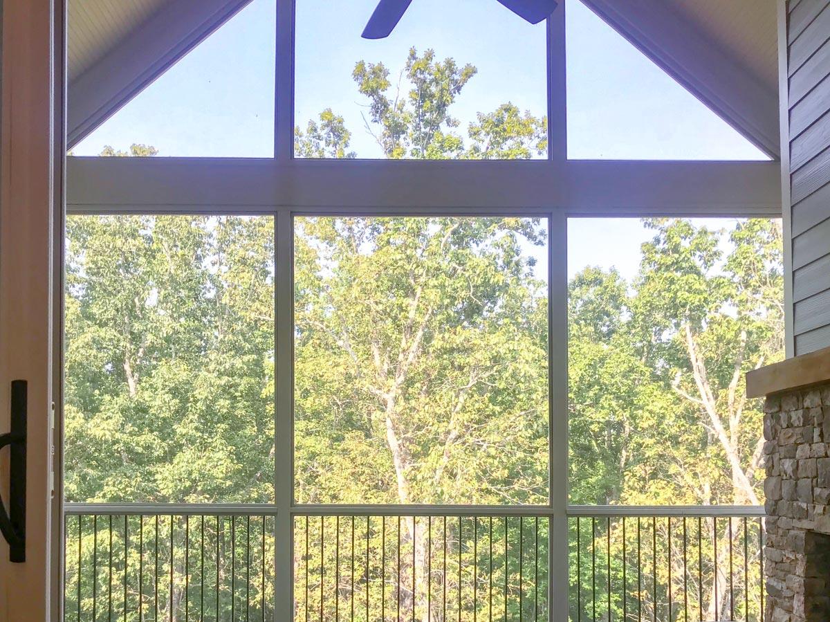 Interior view of great room with vaulted ceiling, large windows, and stone fireplace overlooking trees.