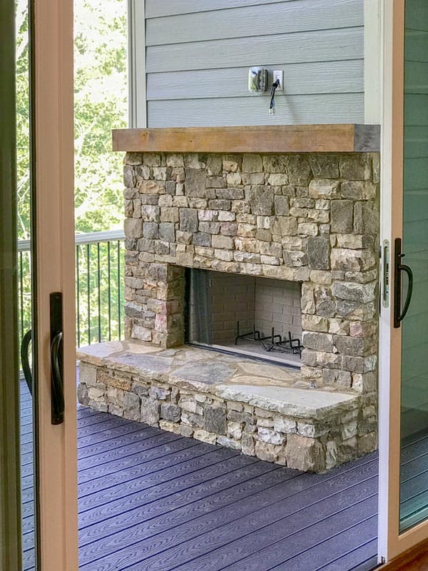 Exterior fireplace with stone hearth and surround, wooden mantel, and dark composite decking.