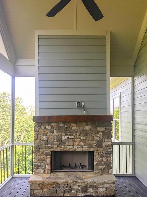 Screened porch with stone fireplace, wood mantel, ceiling fan, and exterior siding.