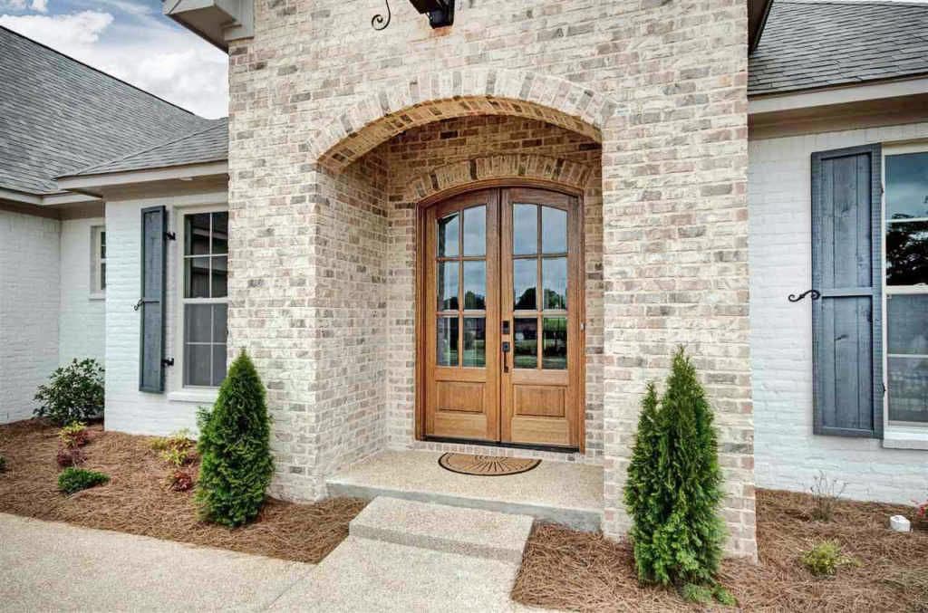 House plan exterior featuring a brick archway over double wooden doors, visible gables, and decorative shutters on white brick.