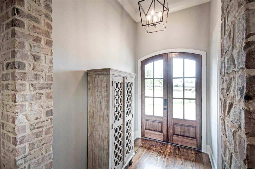 Interior view of entryway with arched double doors, stone accents, decorative cabinet, and geometric pendant light.