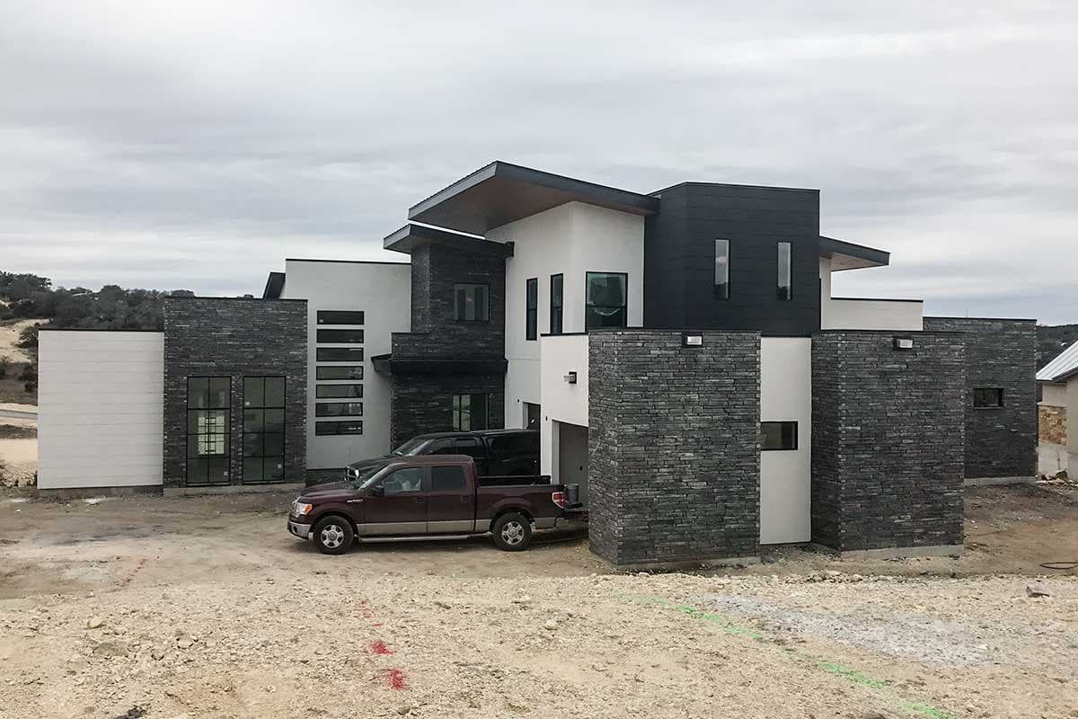 House plan exterior. Modern style with flat rooflines, dark stone accent walls, and an attached garage. Two stories.